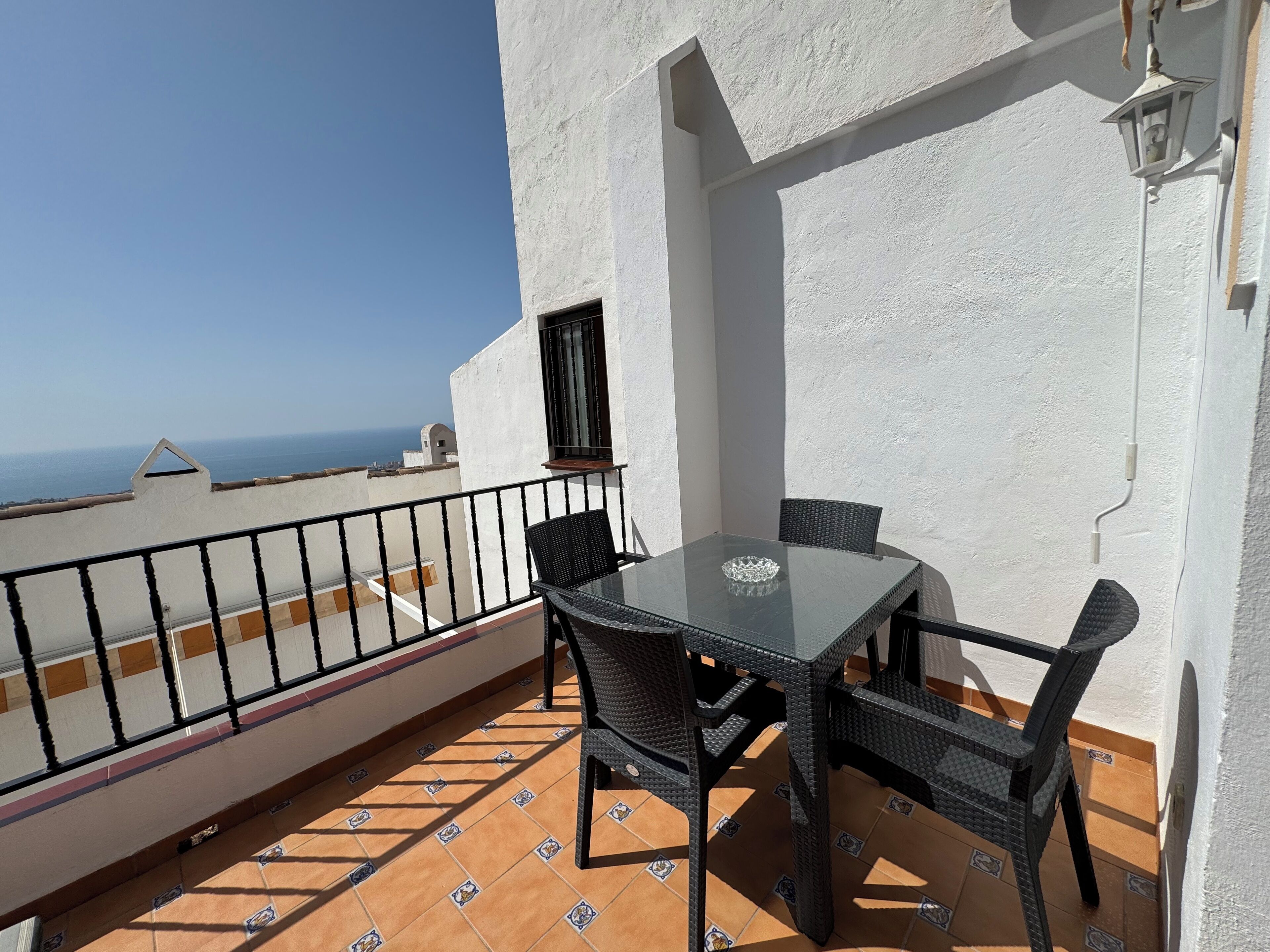 A balcony with a table and chairs, a view of the sea, and a white wall.