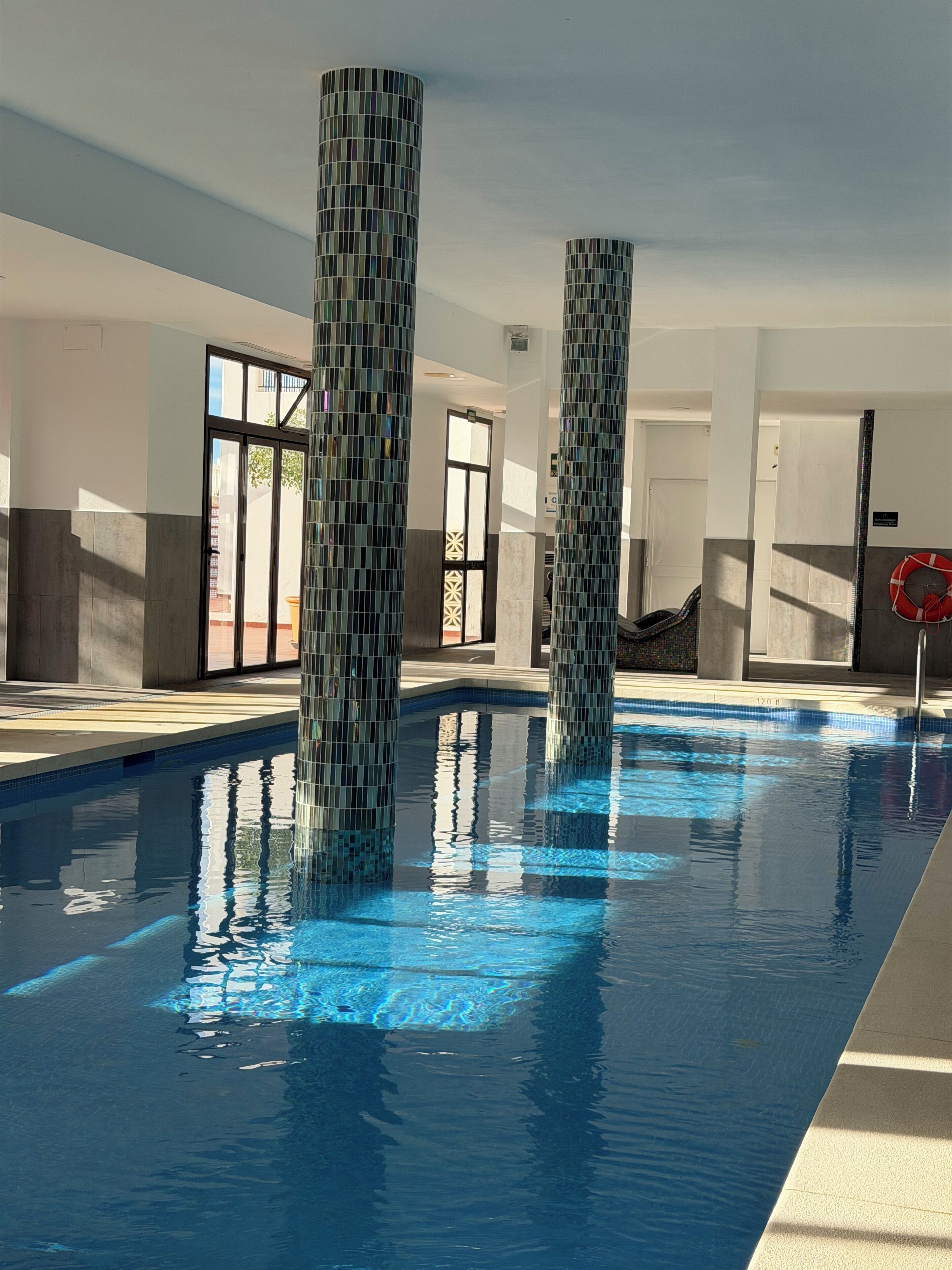 Une piscine avec des piliers recouverts de carreaux, une eau claire et une bouée de sauvetage sur la droite.