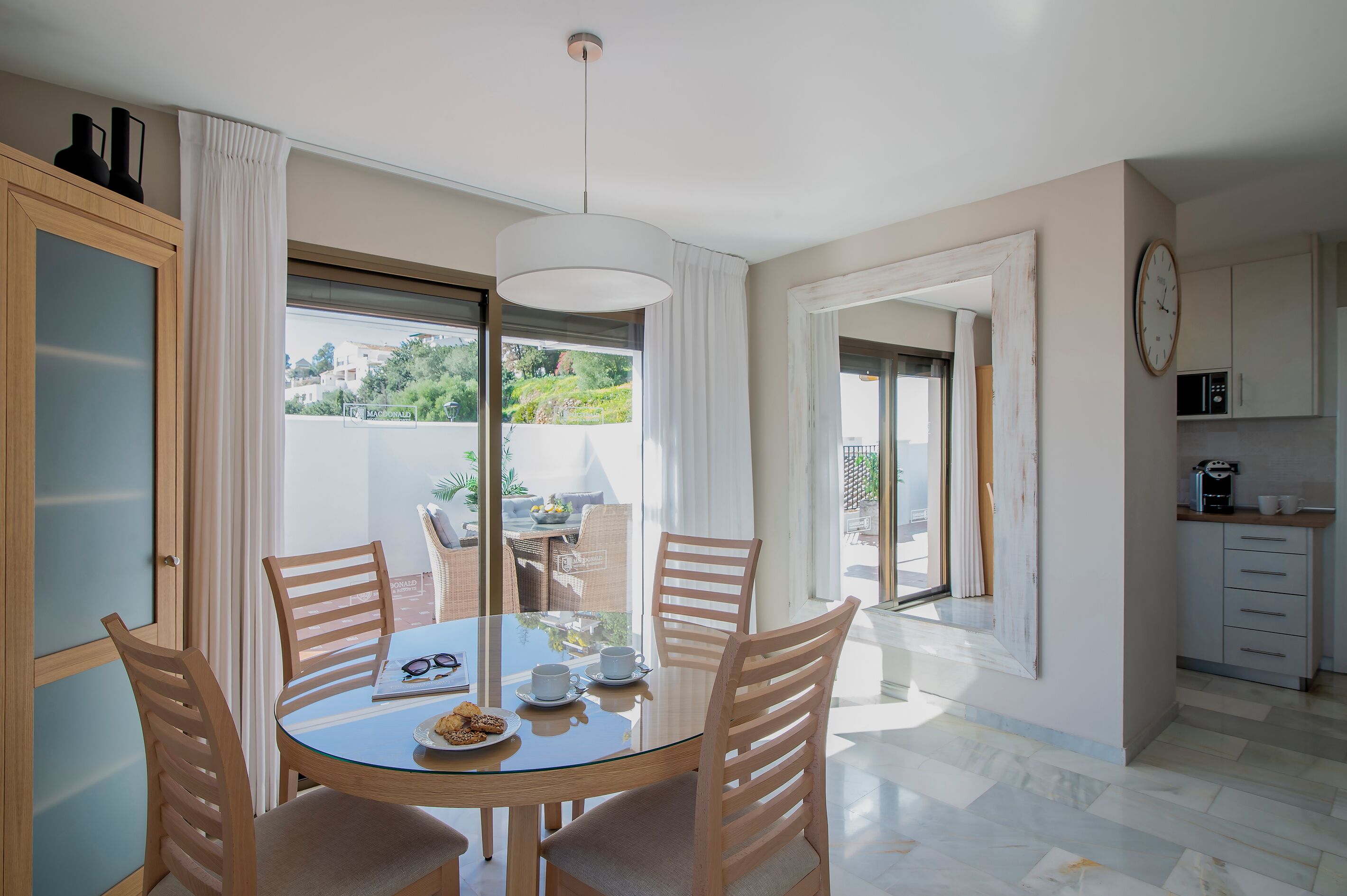 A modern dining area with a glass table, wooden chairs, and a view of the outdoors.