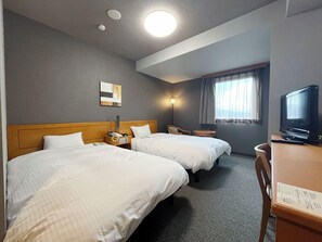 Ein Hotelzimmer mit zwei Betten, einem Schreibtisch mit Fernseher, einer Lampe und einem Fenster mit Vorhängen.