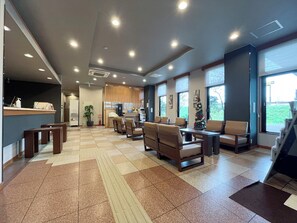 Eine geräumige Lobby mit einer Rezeption, einer Sitzecke und großen Fenstern mit Blick ins Freie.