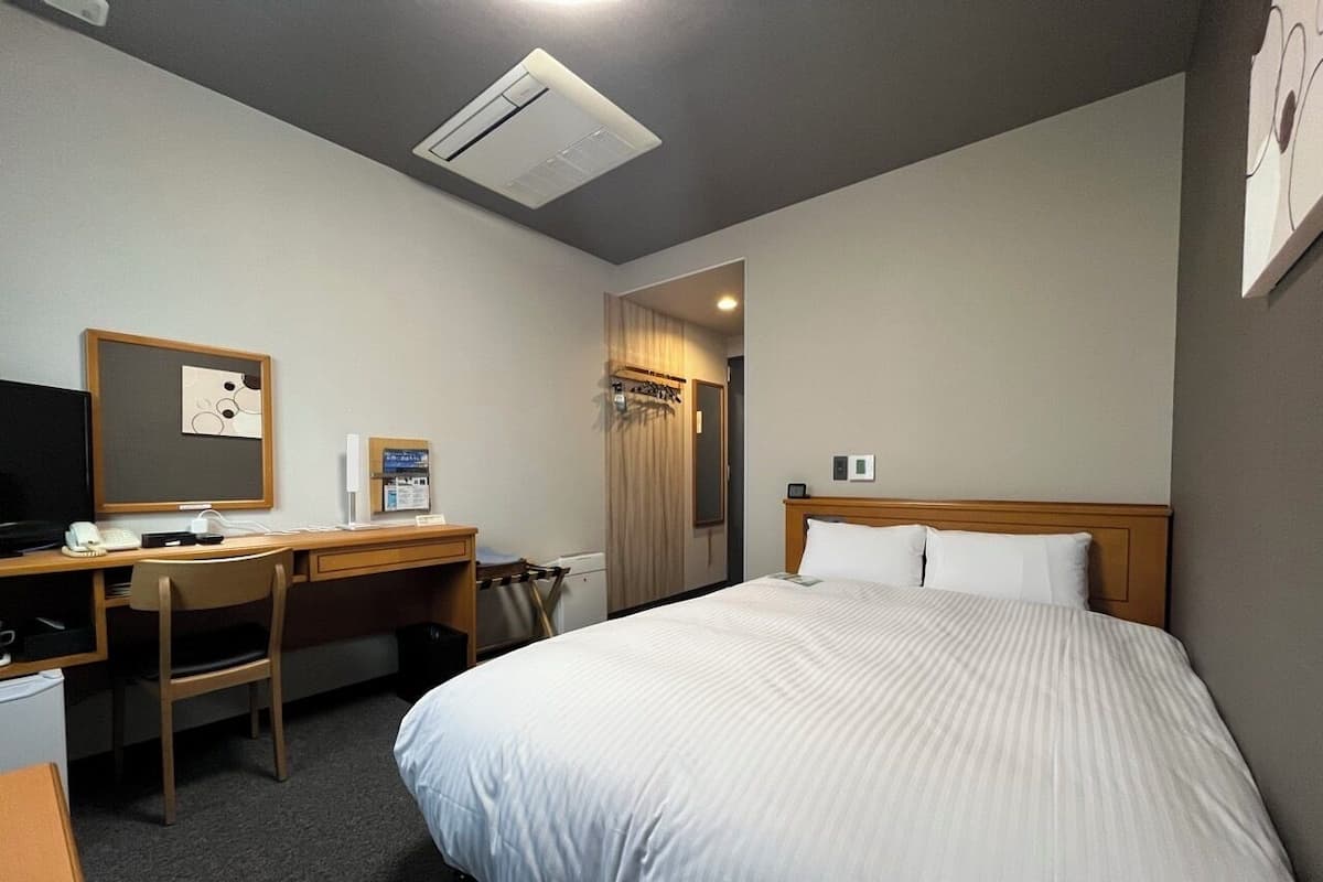Habitación de hotel con cama, escritorio, silla, televisor y puerta que da a un baño.