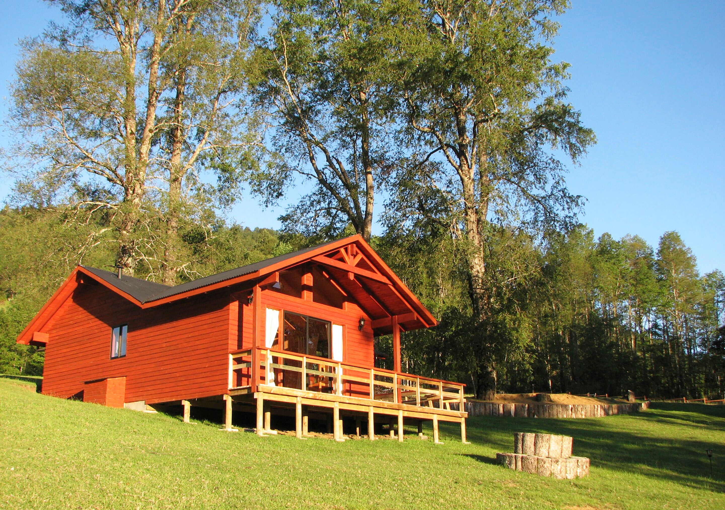 Eine rote Holzhütte mit einem Balkon, umgeben von einer grünen Wiese und Bäumen.