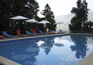 A swimming pool with lounge chairs and umbrellas, surrounded by trees and mountains in the background. - Mirador Los Volcanes Lodge & Boutique (Pucón)