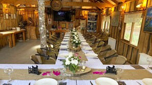 A long dining table set for a meal with chairs on both sides, a wooden interior, and a television in the background. - Mirador Los Volcanes Lodge & Boutique (Pucón)