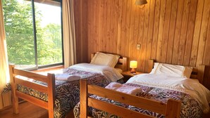 A wooden room with two beds, each with patterned bedding, a window with curtains, and a lamp on the nightstand. - Mirador Los Volcanes Lodge & Boutique (Pucón)