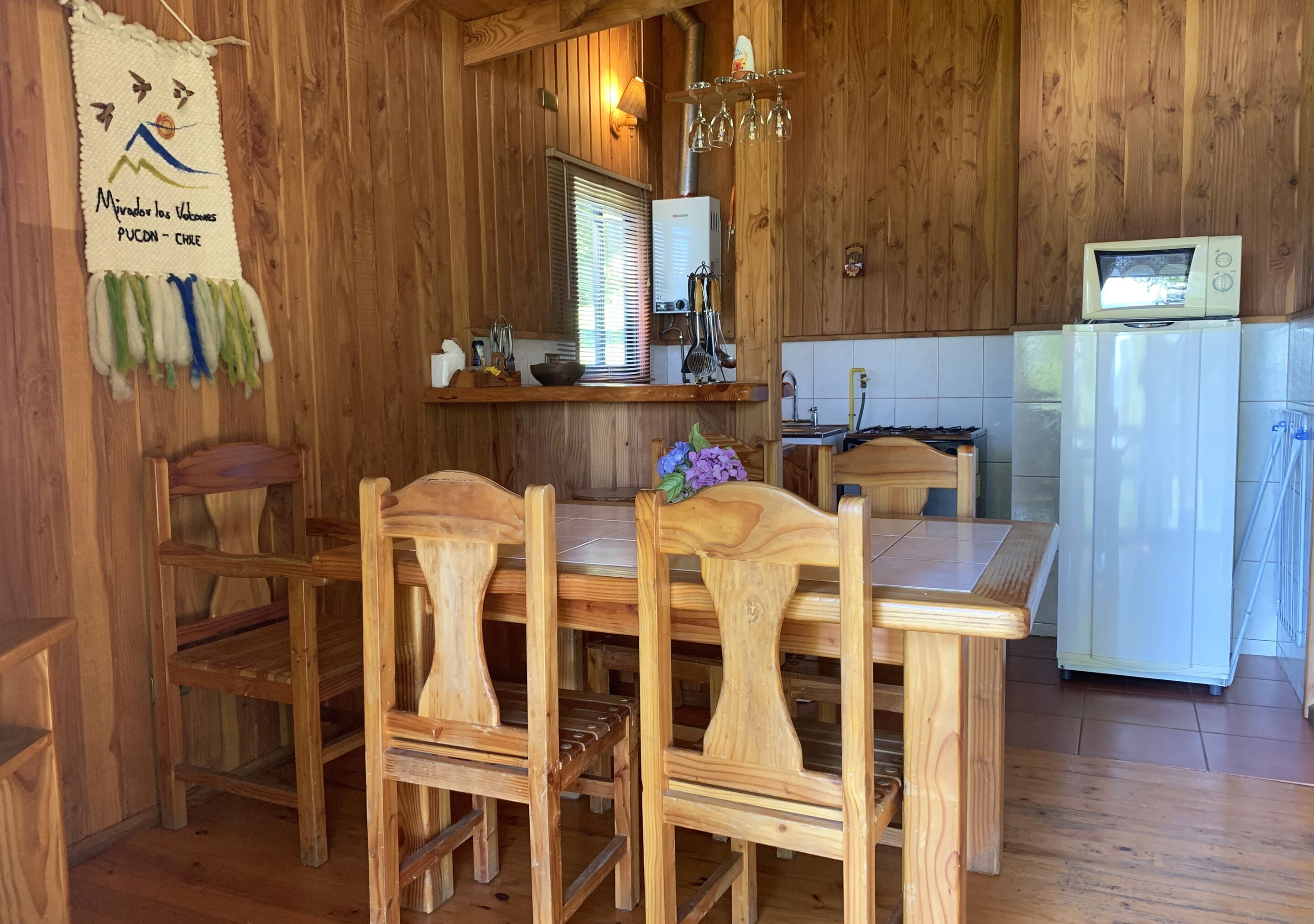Interior em madeira com uma mesa de jantar e cadeiras, um frigorífico branco e um aquecedor fixado na parede.