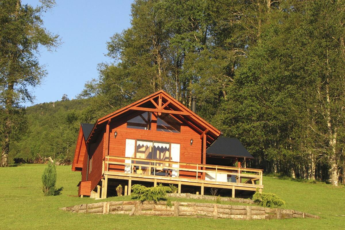 Une cabane en bois dotée d’un balcon, entourée d’une clôture en bois et d’une végétation luxuriante.