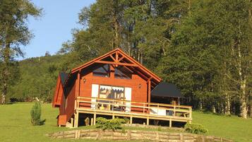A wooden cabin with a balcony, surrounded by a wooden fence and lush greenery.