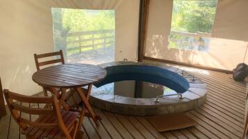 A tent with a wooden table and chairs, a hot tub, and a view of the outdoors.