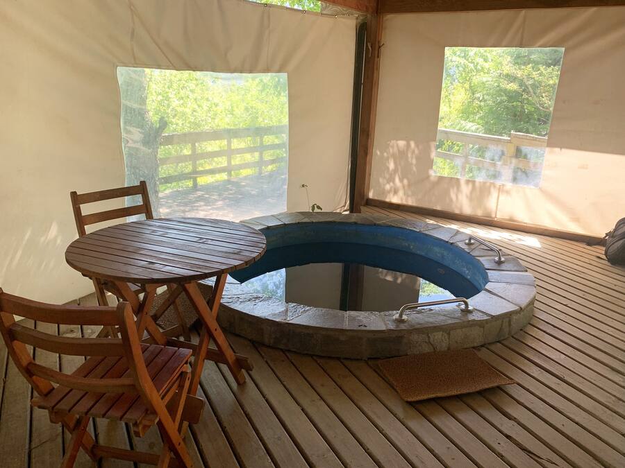 Una tienda de campaña con una mesa y sillas de madera, un jacuzzi y vistas al exterior.