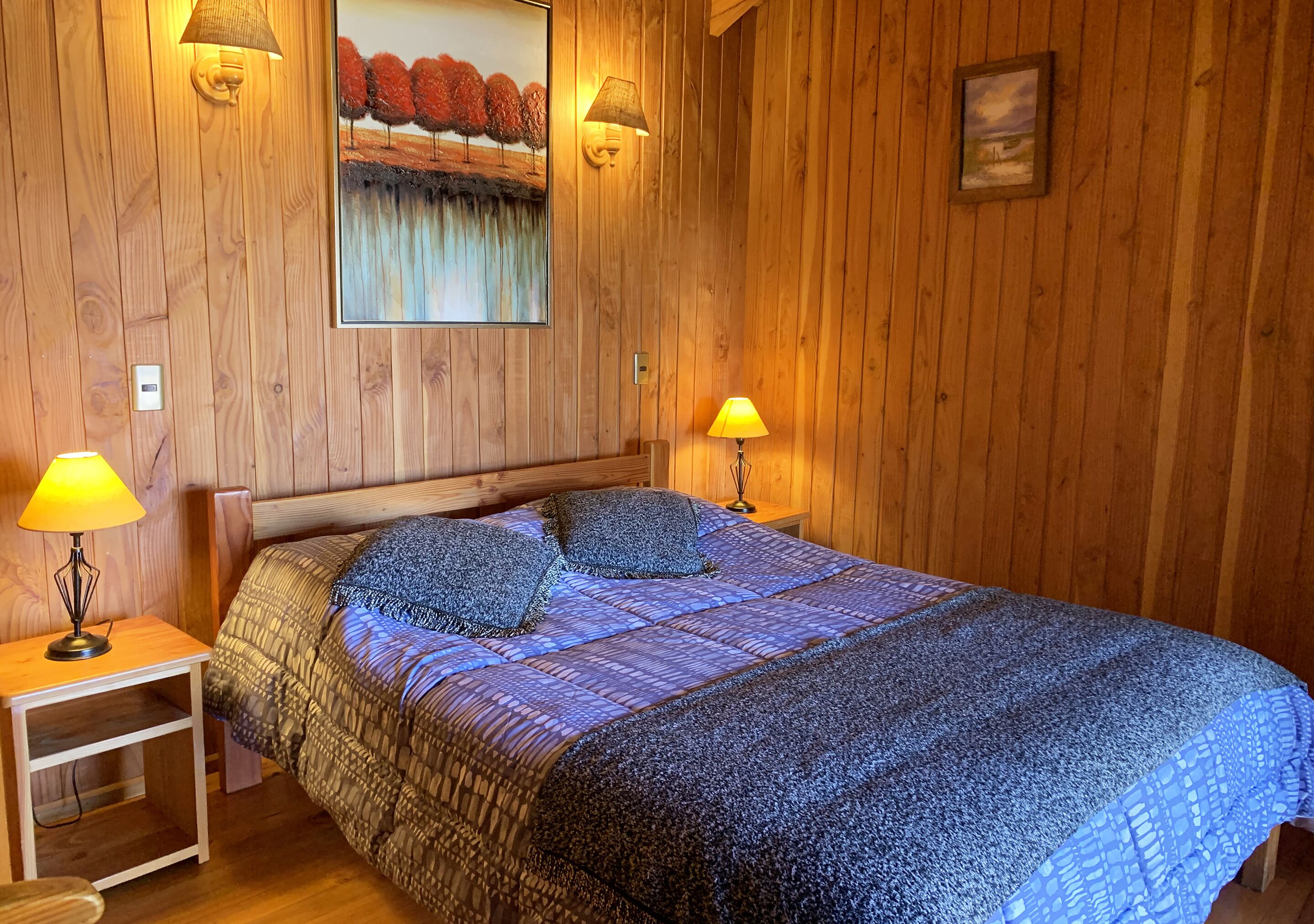 Una habitación con paneles de madera, una cama grande, dos lámparas de noche y un cuadro en la pared.