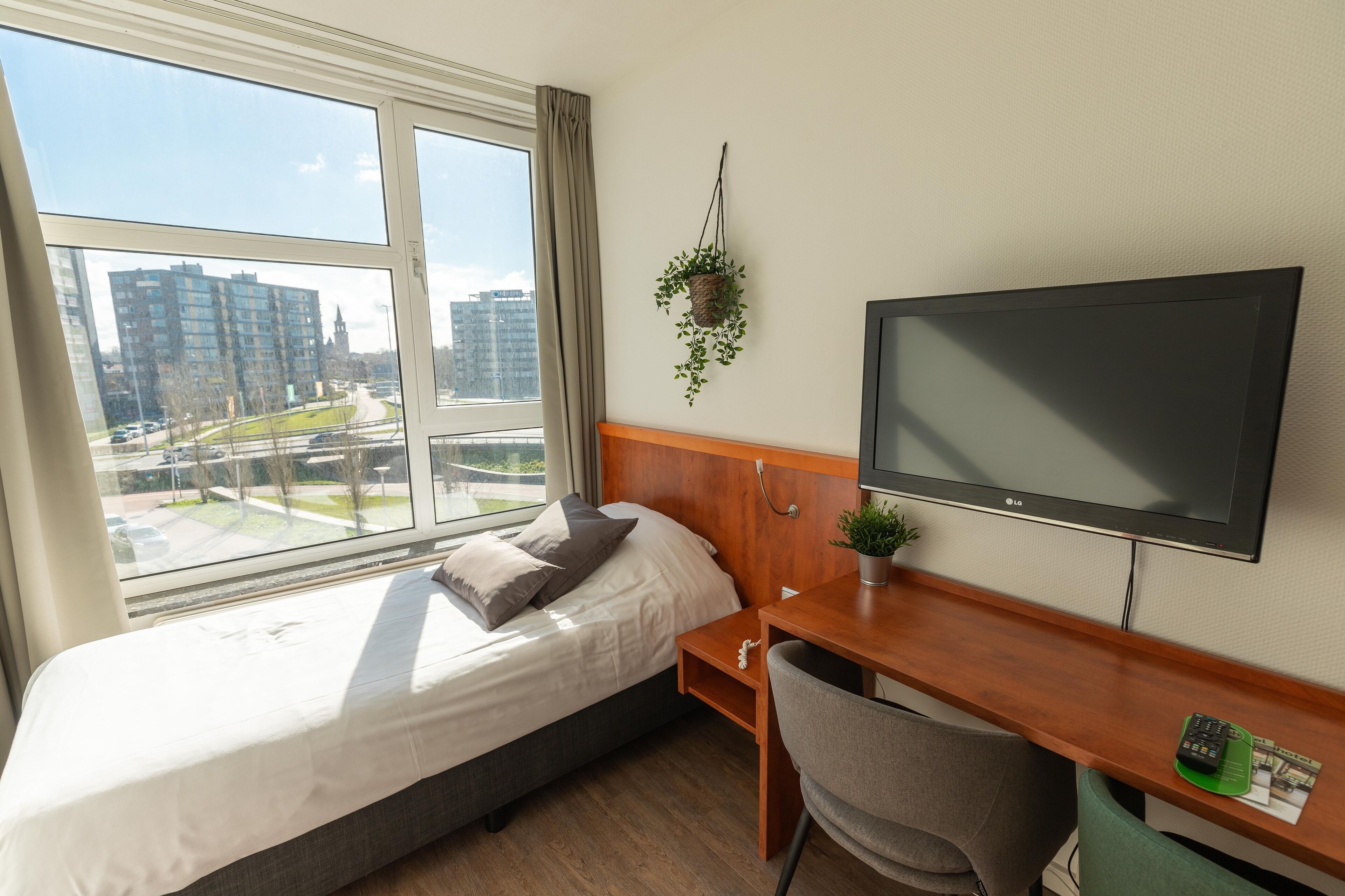 Habitación de hotel con cama, escritorio, silla, televisor y ventana con vista a la ciudad.