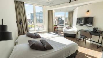 A hotel room with two beds, a desk, a chair, a TV, and large windows offering city views.