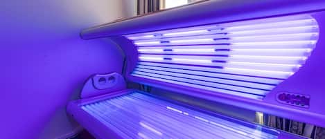 A tanning bed with a control panel, located in a room with a window and curtains.