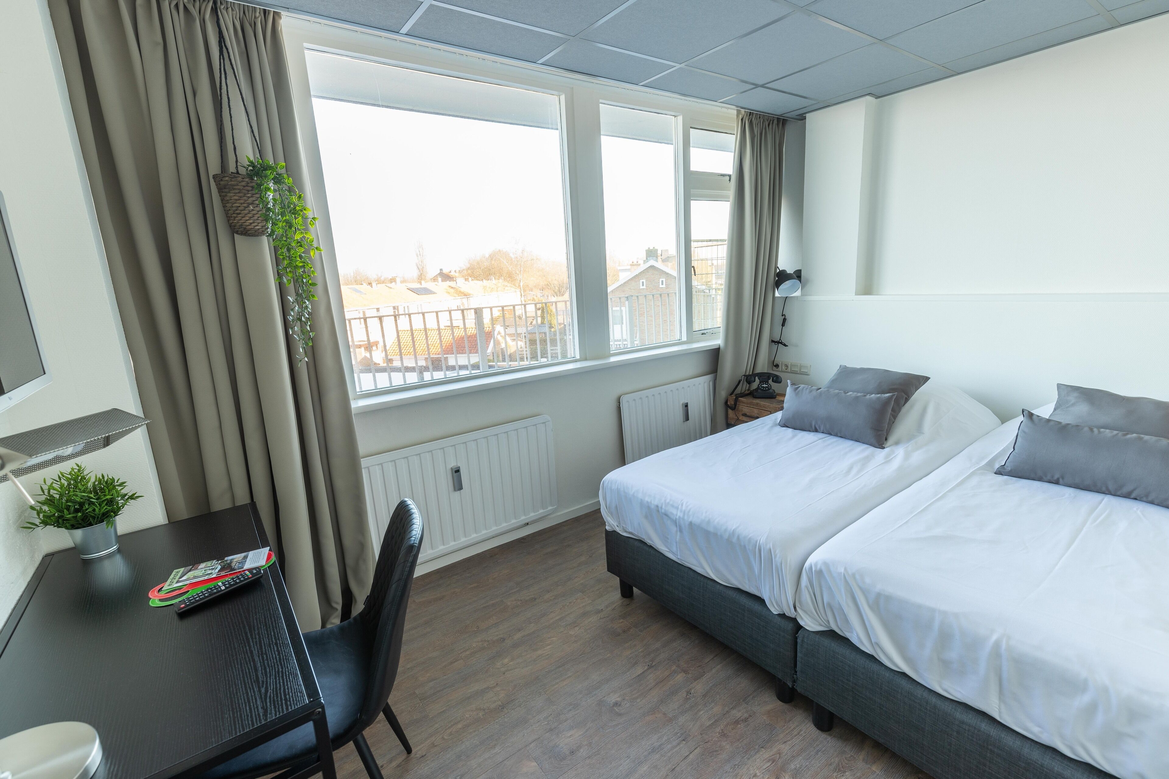 Un dormitorio con cama, un escritorio con planta, una silla y una ventana con cortinas.