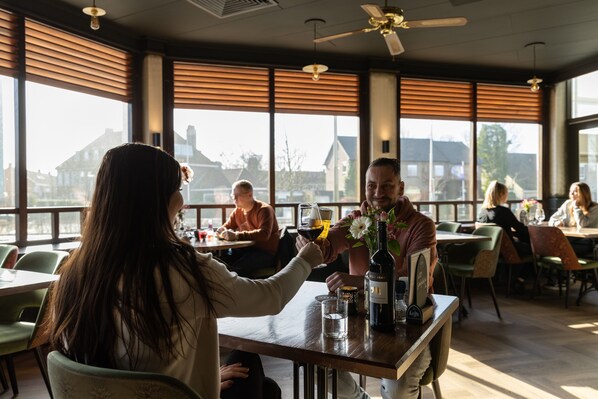 A restaurant with large windows, wooden blinds, and a ceiling fan.