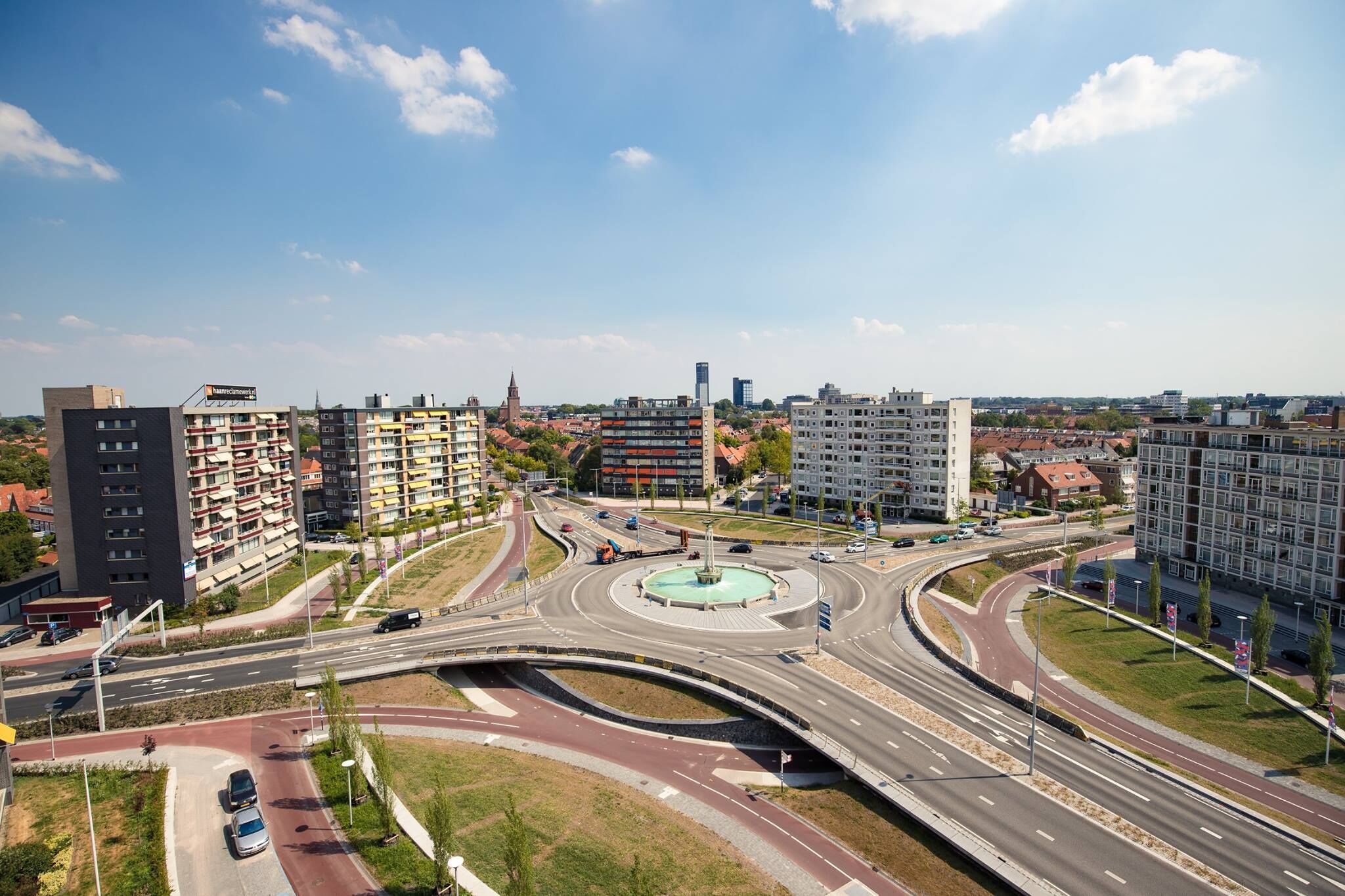 Un nudo vial urbano de varios niveles con edificios modernos, una rotonda central y múltiples carreteras.