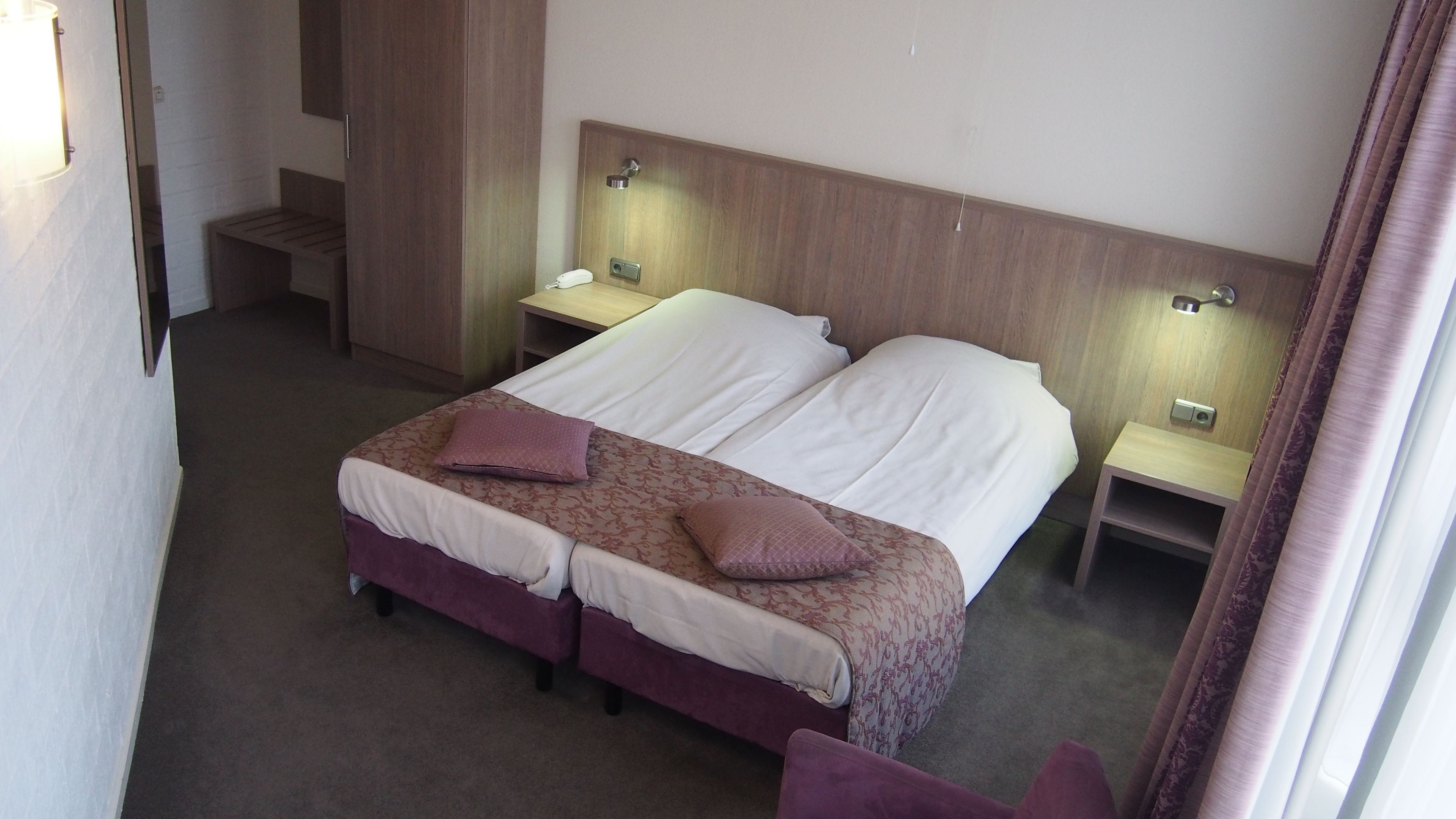 Una cama doble con dos almohadas, un cabecero de madera, dos mesitas de noche con lámparas y suelo cubierto de alfombra.