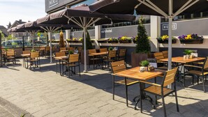 Ein Straßencafé mit Holztischen und -stühlen, Sonnenschirmen und Blumenkästen.