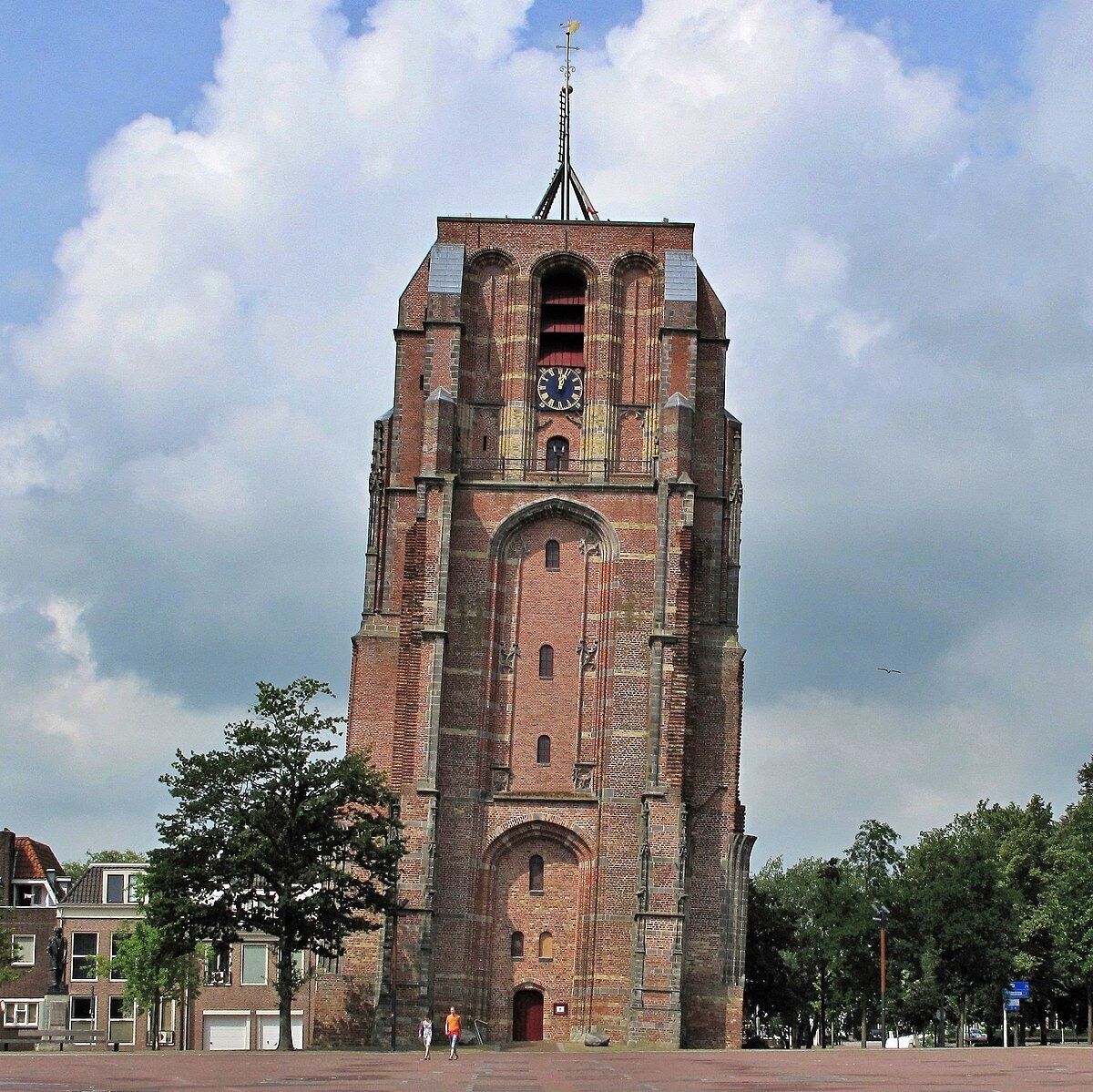 A large brick tower with a clock and a weather vane on top.