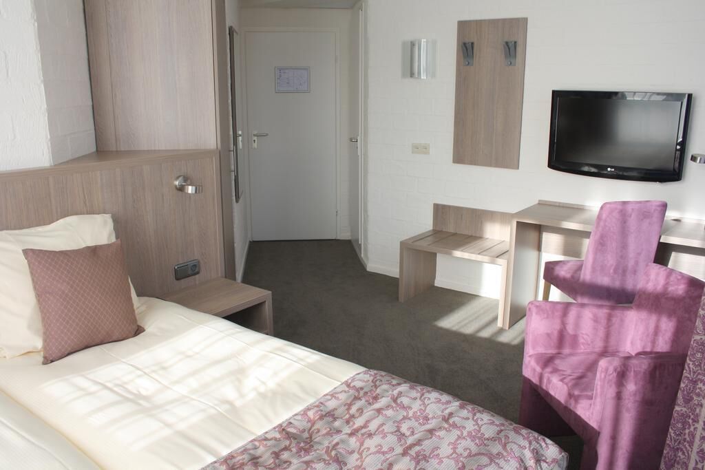 Una habitación de hotel con cama, escritorio, silla, televisor y armario.