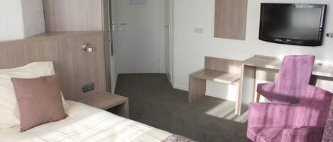 A hotel room with a bed, a desk, a chair, a television, and a wardrobe.