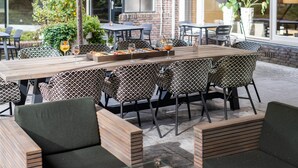 Un área de comedor al aire libre con una larga mesa de madera, sillas estampadas y asientos acolchados.