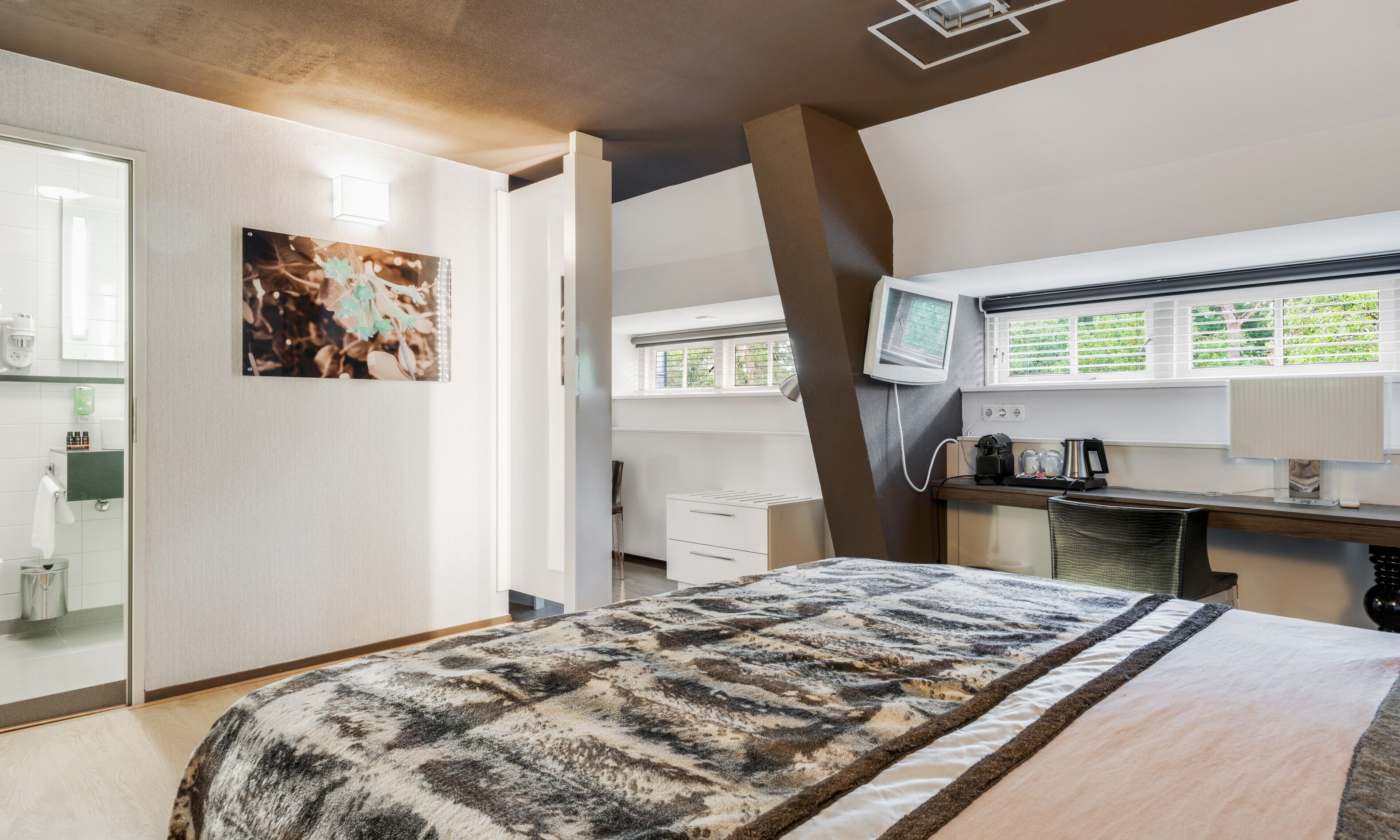 Ein Hotelzimmer mit Bett, Schreibtisch, Fernseher und einem Fenster mit Jalousien.