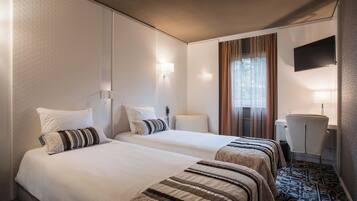 A hotel room with two beds, a desk, a chair, a television, and a window with curtains.
