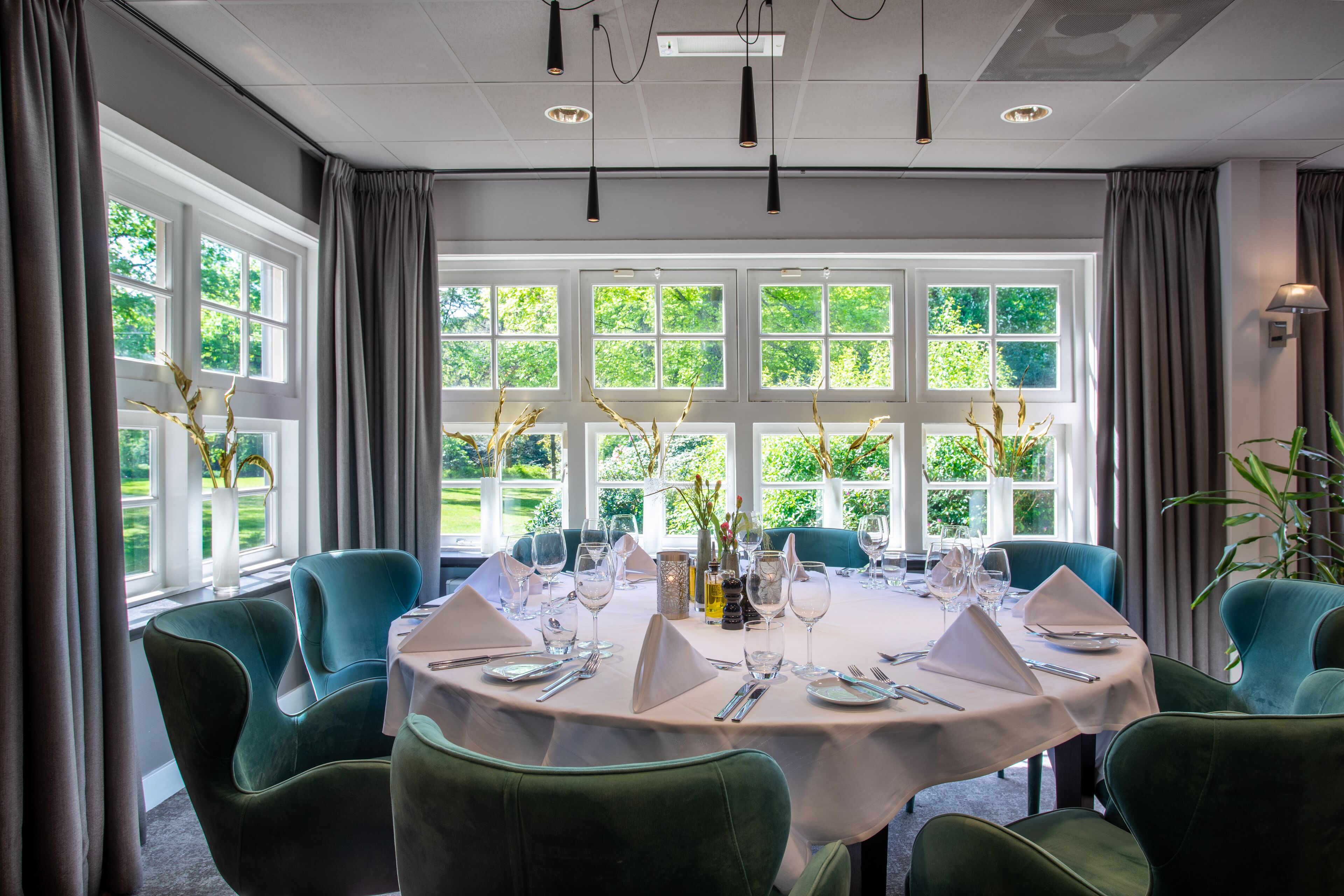 A dining area with a round table set for six, surrounded by green upholstered chairs.