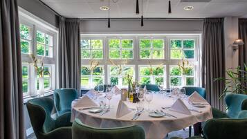 A dining area with a round table set for six, surrounded by green upholstered chairs.