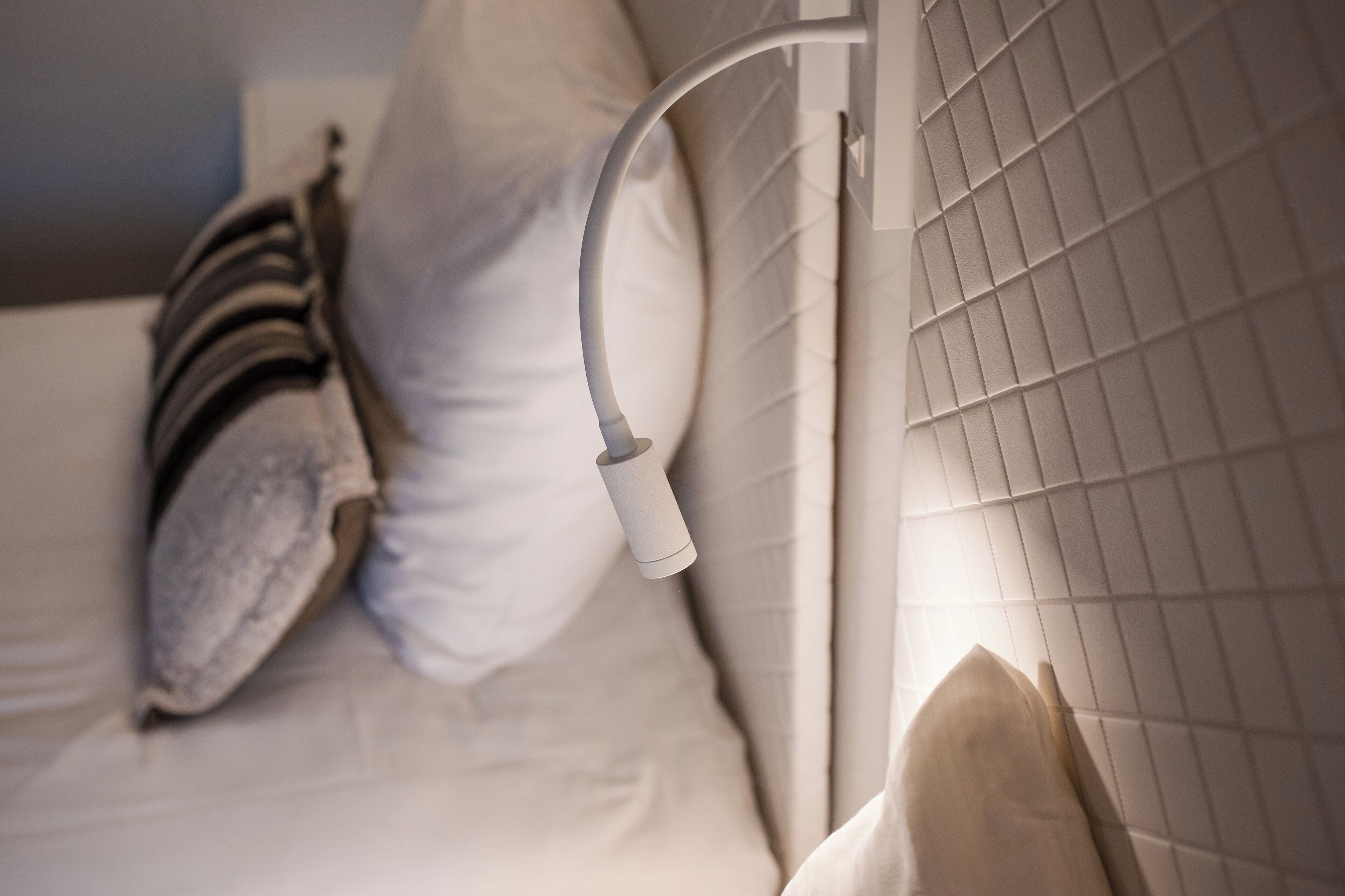Un lit bien fait, avec une literie blanche, un oreiller et une table de chevet sur laquelle se trouve une lampe.