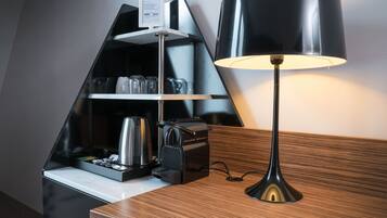 Een moderne keuken met een koffieapparaat, een waterkoker en een koffiekan op een aanrecht. Er staat een zwarte lamp met een witte lampenkap op een houten tafel.