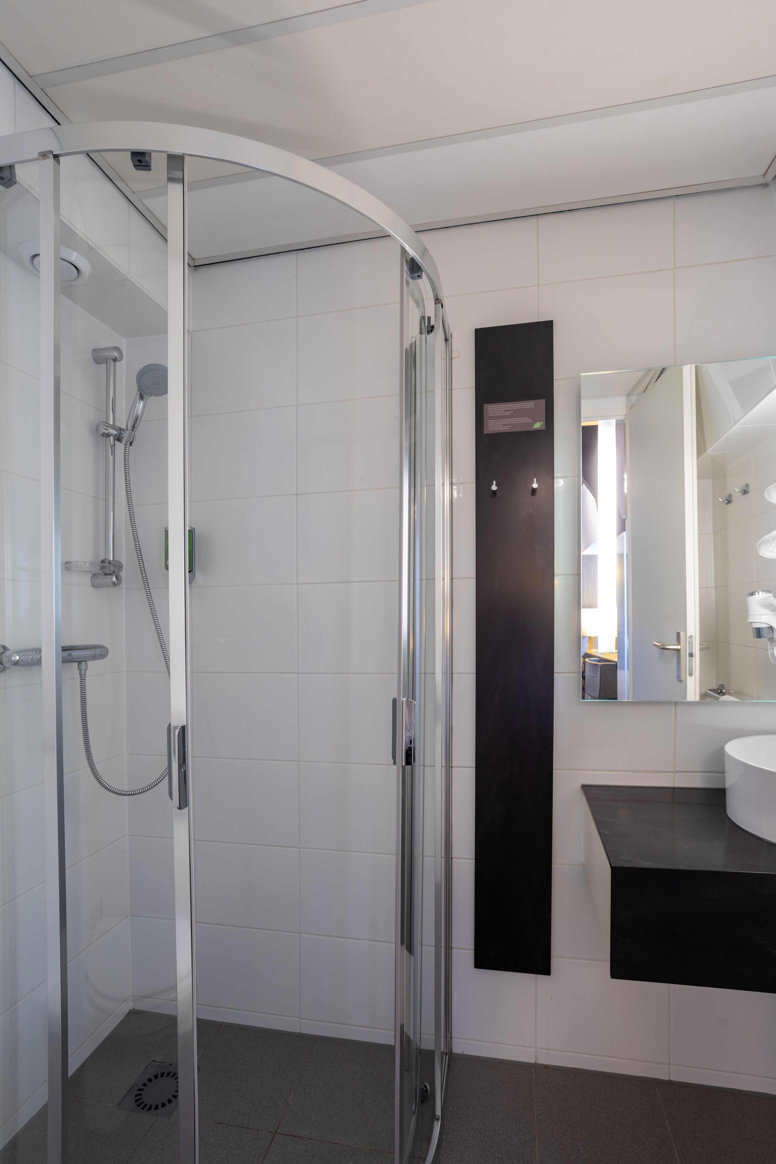 A modern bathroom with a glass-enclosed shower, a black sink vanity, and a large mirror.