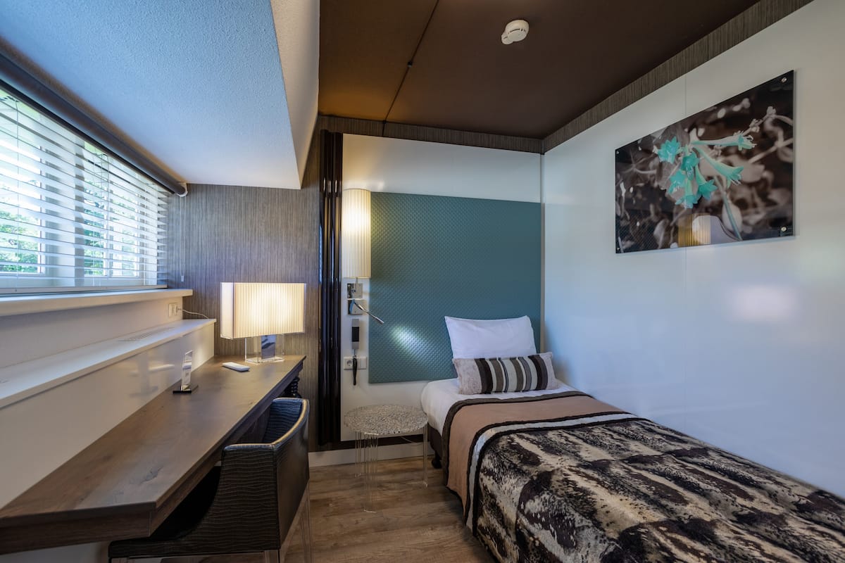 Una habitación de hotel moderna con cama, mesita de noche, lámpara y un cuadro en la pared.