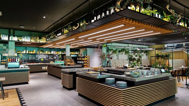 Un café moderno con mostradores de madera, diversas bebidas y plantas colgantes.