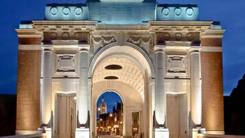 A grand, illuminated archway with classical architectural elements, leading into a cityscape at dusk.