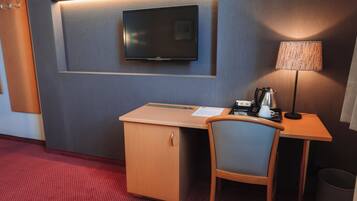 Een hotelkamer met een bureau, stoel, televisie, lamp en een prullenbak.