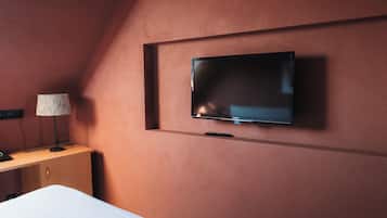 Une pièce avec un téléviseur fixé au mur, un bureau avec une lampe et un lit.