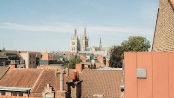 Vista de tejados con tejas de barro, la aguja de una iglesia a lo lejos y un cielo azul despejado.