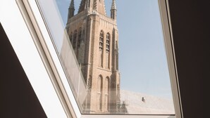A skylight window with a view of a historic building with a pointed tower. - Albion Hotel (Ypres)