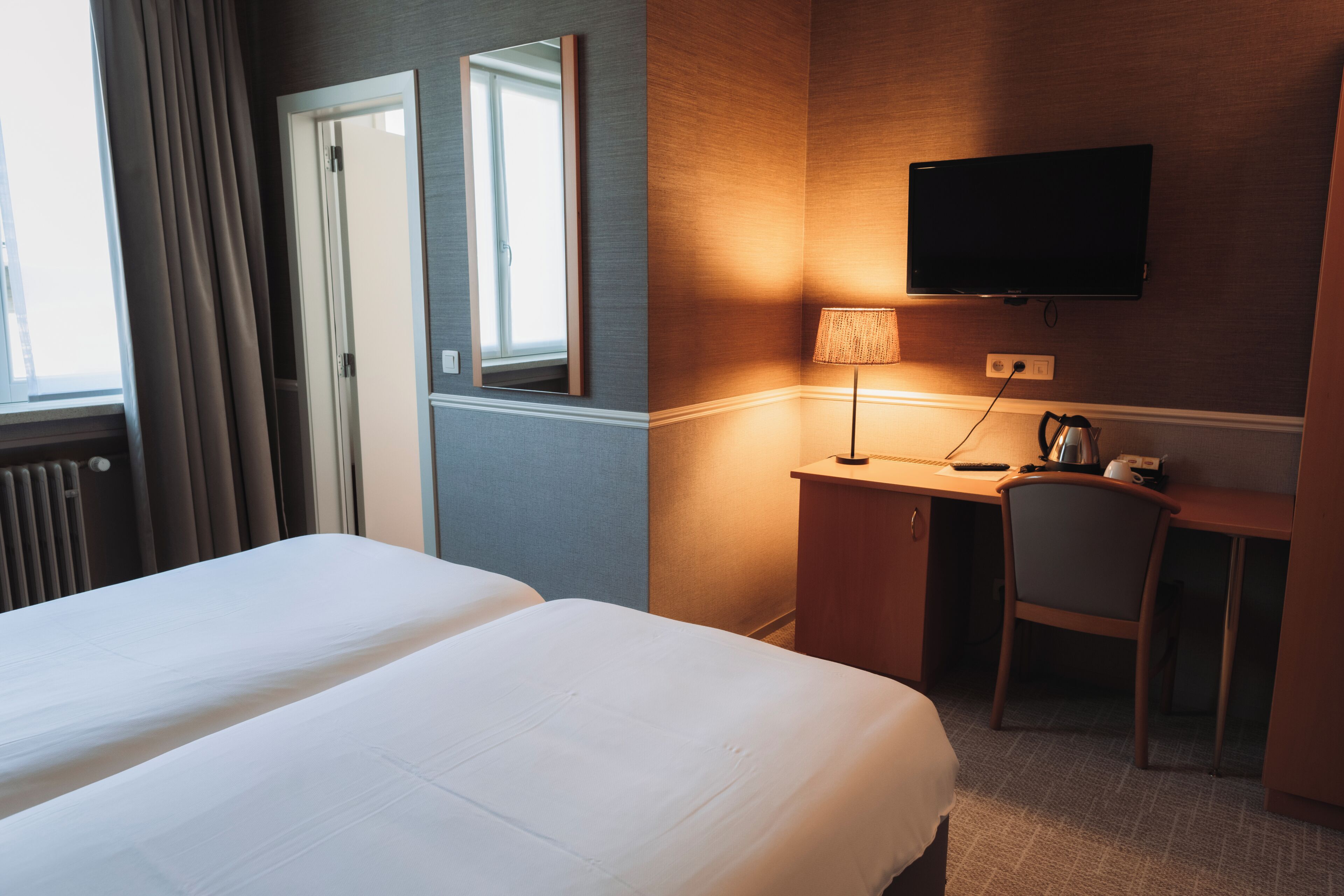 Habitación de hotel con dos camas, un escritorio con silla, televisión y ventana con cortinas.