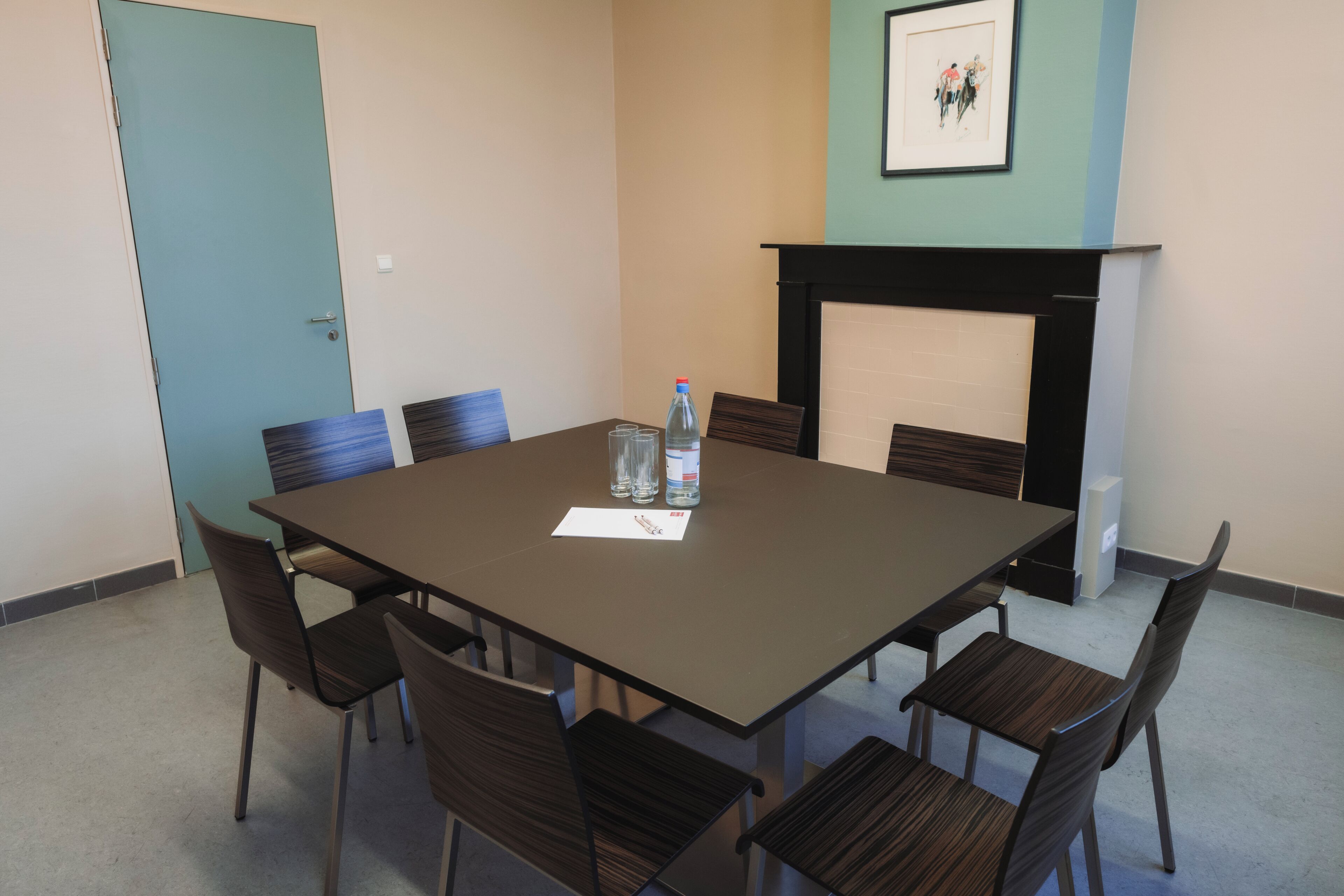 A conference room with a rectangular table, six chairs, a water bottle, a glass, and a framed picture on the wall.