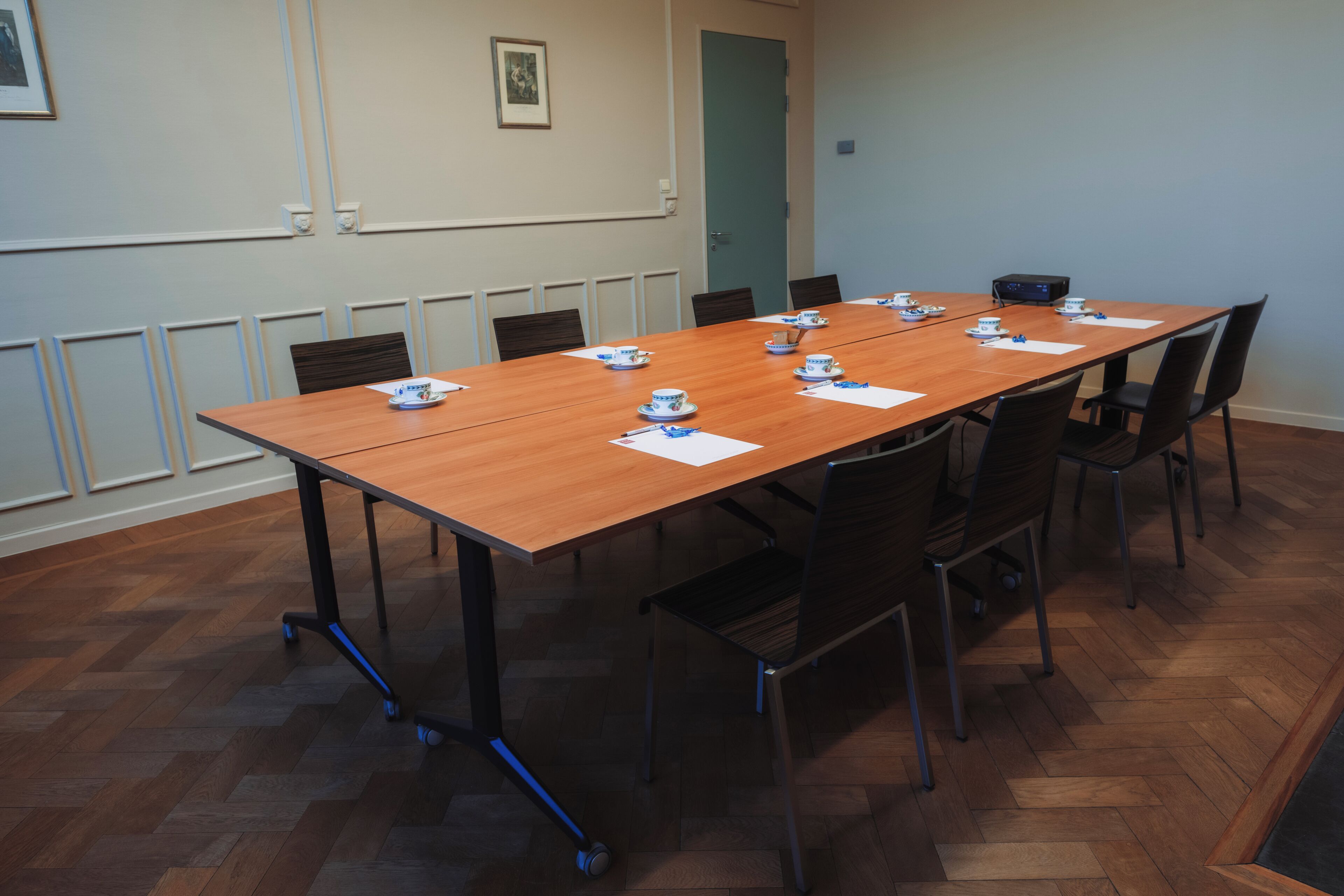 A conference room with a wooden table, chairs, a projector, and a door.