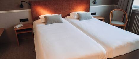 A hotel room with two beds, a nightstand with a phone, a chair, and a wall-mounted lamp.