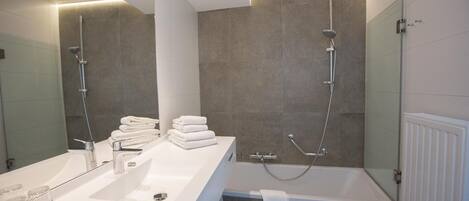 Un baño moderno con un lavamanos grande de color blanco, una mampara de ducha de cristal y una bañera.