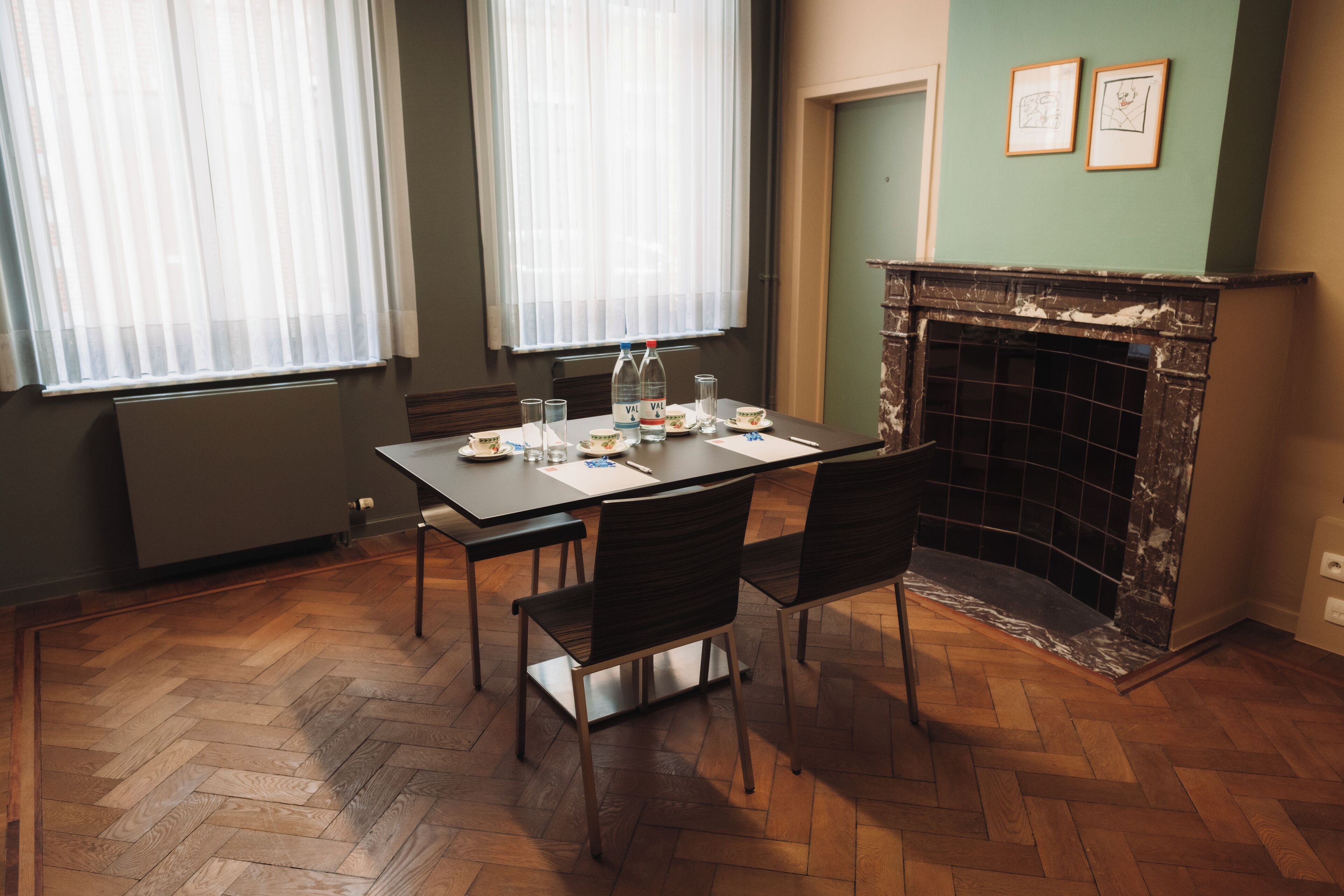 A room with a dining table set for four, a fireplace, and two windows with sheer curtains.