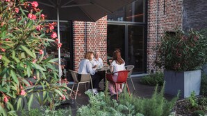 An outdoor seating area with brick walls, a glass door entrance, and surrounding greenery. - Albion Hotel (Ypres)