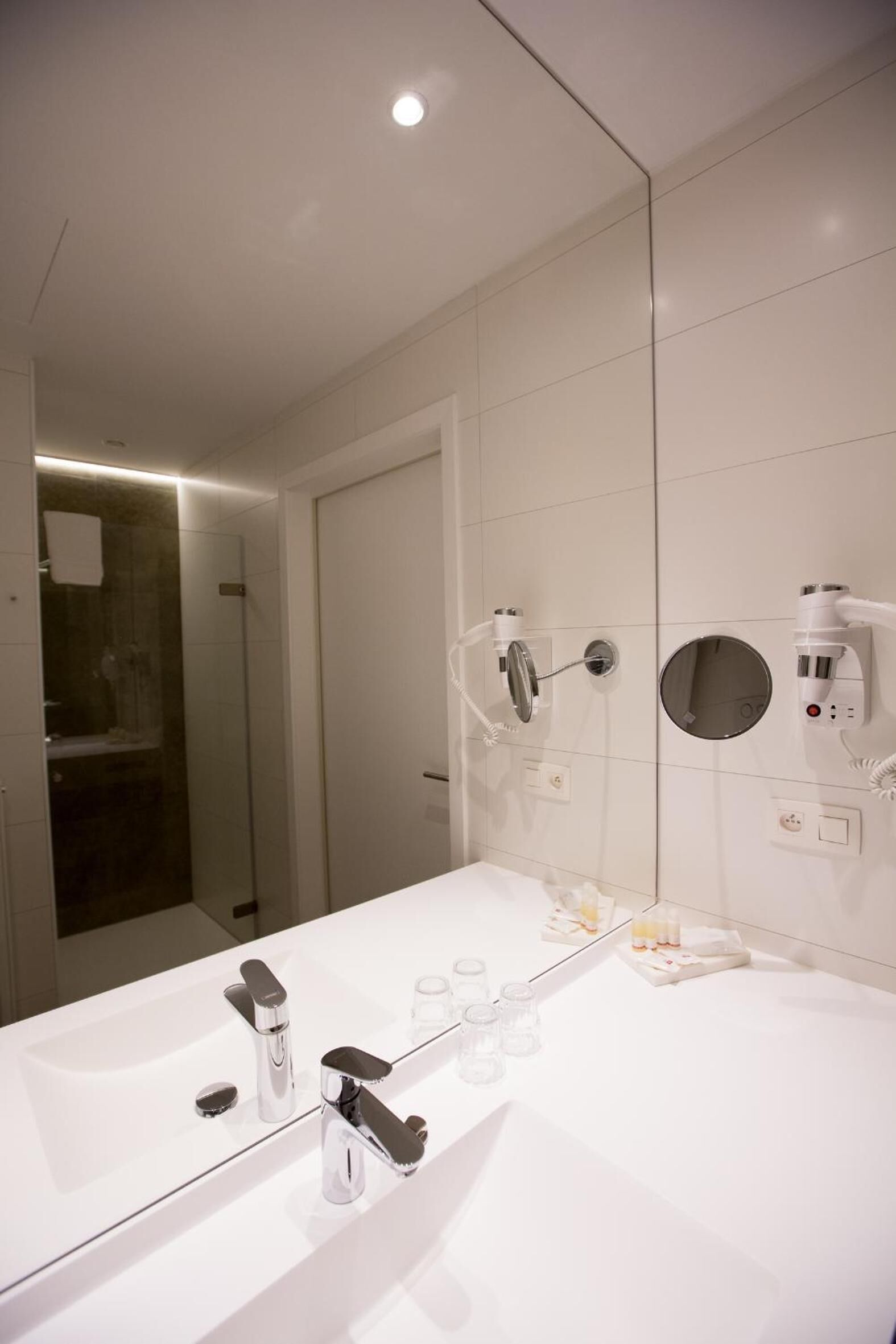 A modern bathroom with a large mirror, two sinks, and a hairdryer mounted on the wall.